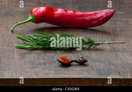 Poivron rouge frais, branche de romarin, cuillère de mesure de piment rouge moulu spice sur dark, planche à découper en bois. Banque D'Images