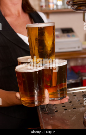 Serveuse habile équilibre entre quatre verres de bière Banque D'Images