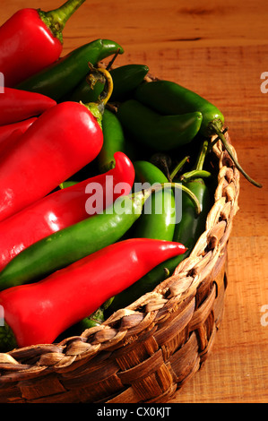 Libre d'un assortiment de Poivrons et piments dans un panier en osier sur une surface en bois rustique. Format vertical. Banque D'Images