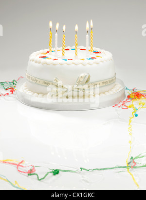 Un gâteau d'anniversaire blanche avec la lumière des bougies et de banderoles Banque D'Images