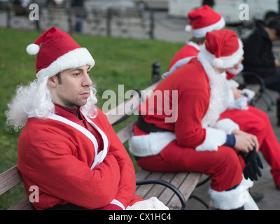 Un père Noël est assis sur un banc de parc avec d'autres Santas pendant Santa Con, un pub crawl annuel avec des milliers habillé en père Noël Banque D'Images