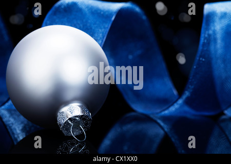 Bal de noël argent mat en face d'un ruban bleu sur noir fond réfléchissant Banque D'Images