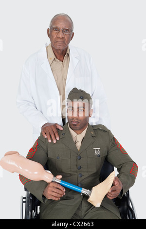 Portrait de senior doctor avec nous officier militaire holding membre artificiel comme il est assis en fauteuil roulant sur fond gris Banque D'Images