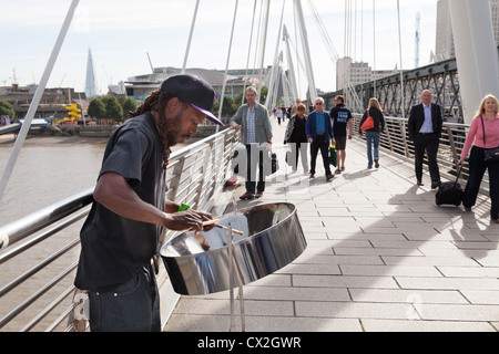 Musicien ambulant jouant le steel band drum (tambour métallique) sur le Jubilé passerelle au-dessus de la Tamise par Hungerford Bridge Banque D'Images