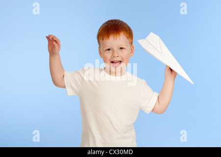 Adorable garçon roux avec paper plane modèle sur fond bleu en studio Banque D'Images