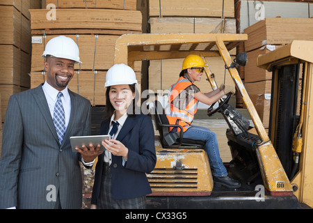 Heureux les ingénieurs multiethnique holding tablet PC avec travailleur féminin roulant chariot élévateur en arrière-plan Banque D'Images