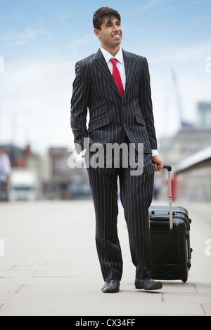 Young Indian businessman pulling luggage bag on street Banque D'Images