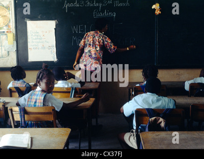 St Kitts Basseterre Caraïbes enfants à l'École de classe avec female teacher Writing On Blackboard Banque D'Images