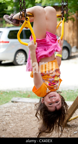 Petite fille à l'envers accroché de trapeze de grimpeurs. Banque D'Images