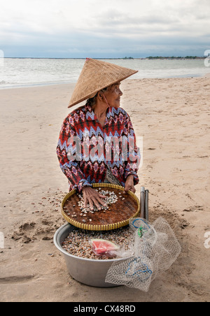 Femme la collecte des coquillages pour faire des colliers. Sur la plage de Jimbaran, péninsule de Bukit, au sud de Bali, Indonésie. Banque D'Images