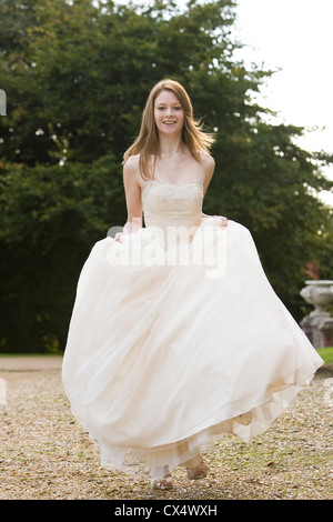 Jeune femme en robe nuptiale crème sur le chemin de gravier à marcher vers la caméra et jupes holding smiling Banque D'Images