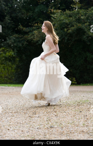 Vue de côté de jeune femme en robe de mariée crème holding jupes en raison de stately home Banque D'Images