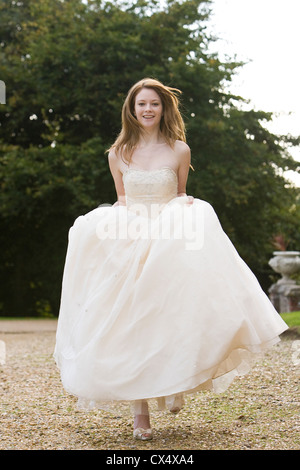 Jeune femme en robe de mariée crème à marcher vers la caméra en jupes motifs de stately home Banque D'Images