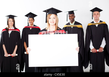 Pretty female graduate holding white board avec ses camarades en arrière-plan Banque D'Images