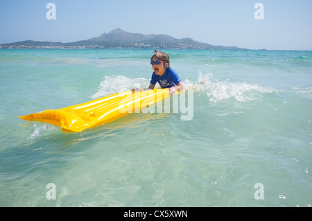 Un jeune garçon s'amusant à jouer dans les vagues sur un radeau gonflable lilo Banque D'Images