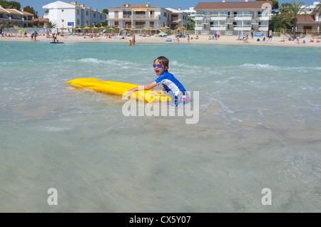 Un jeune garçon palettes dans la mer chaude sur un radeau gonflable lilo jaune Banque D'Images