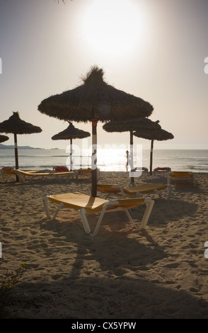 Un coureur solitaire sur une plage vide comme le soleil se lève passé en courant des chaises longues et des chaises Banque D'Images