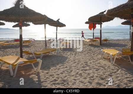 Un coureur solitaire fonctionne sur le sable doré de la plage d'Alcudia passé les parasols et chaises Banque D'Images