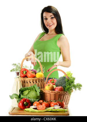 Young smiling woman standing à la table avec variété de légumes crus dans des paniers en osier isolated on white Banque D'Images