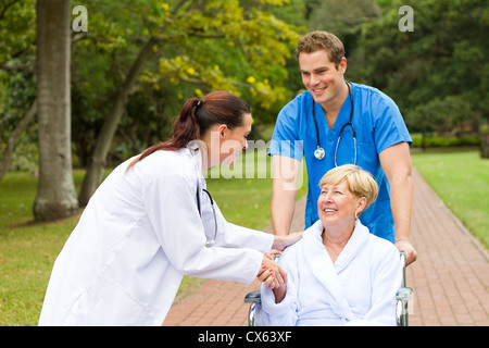 Friendly female doctor greeting récupération senior patient in wheelchair outdoors Banque D'Images