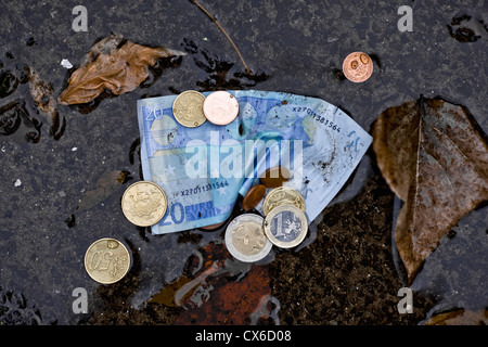 Un billet de vingt euros et des pièces en euros dans une flaque Banque D'Images