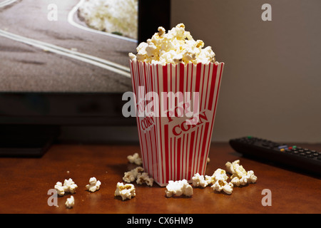 Un carton à rayures rouges de popcorn sur une table en face d'une télévision écran plat Banque D'Images