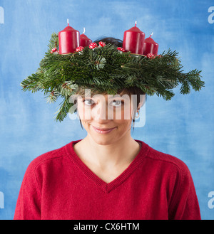 Jolie jeune femme portant la guirlande avec quatre bougies sur sa tête, studio shot noël contre un fond blanc et bleu. Banque D'Images