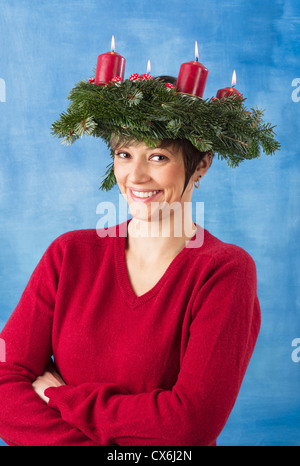 Smiling young woman wearing guirlande sur la tête, quatre bougies sont burning studio shot contre un fond blanc et bleu Banque D'Images