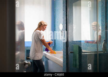 Le ménage et la vie : femme petits travaux dans salle de bains à la maison, nettoyage lavabo et robinet avec détergent spray Banque D'Images