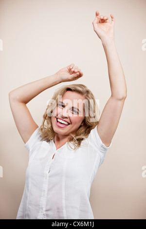 Une jeune femme blonde, bras levés en l'air, smiling Banque D'Images