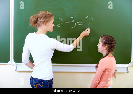Photo de teacher writing on blackboard avec la jolie somme de près de l'élève par Banque D'Images
