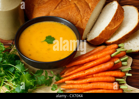 Plat de soupe de coriandre et de carotte fait maison dans la cuisine entouré par des ingrédients et du pain croustillant Banque D'Images