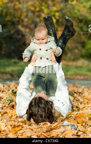 Belle Mère et bébé fils jouant sur les feuilles d'automne Banque D'Images
