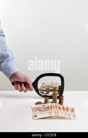 Un homme tenant un miroir à main jusqu'à une pile de monnaie de l'Union européenne Banque D'Images