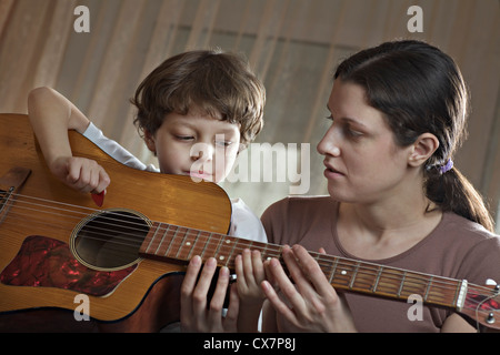 Une mère d'aider son jeune fils jouant avec une guitare acoustique Banque D'Images