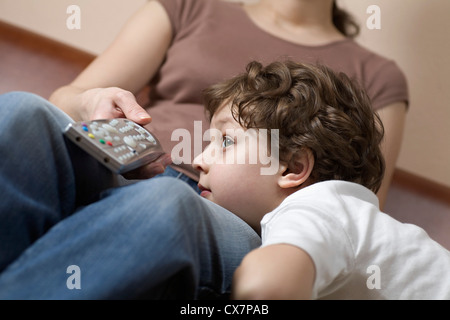 Un jeune garçon se reposant sa tête sur la jambe de sa mère, regarder la télévision Banque D'Images