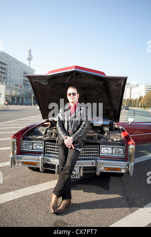 Un endroit frais rockabilly guy holding tools appuyé contre l'avant de sa voiture d'époque, capot Banque D'Images