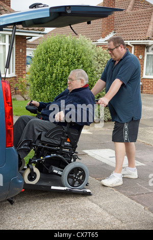 Carer mâle fils de pousser un vieil homme handicapé dans un fauteuil roulant sur un bâti en rampe dans une voiture spécialement adaptés pour se déplacer Banque D'Images