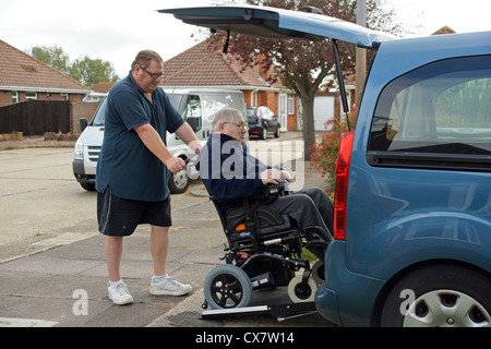 Carer mâle fils de pousser un vieil homme handicapé dans un fauteuil roulant sur un bâti en rampe dans une voiture spécialement adaptés pour se déplacer Banque D'Images