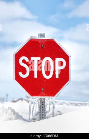 Un panneau d'arrêt avec glaçons pendant de dans alors que presque enterré dans un banc de neige profonde. Banque D'Images