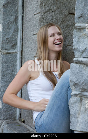 Très jolie jeune femme assise à l'extérieur et reposant dans une fenêtre en pierre avec un rire heureux, Banque D'Images