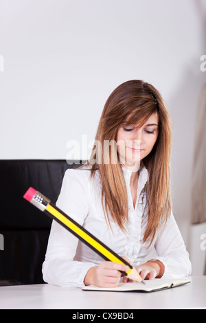 Businesswoman prenant des notes sur son bloc-notes avec un crayon géant Banque D'Images