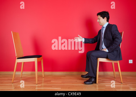 Poignée d'accord entre un homme et une chaise à côté d'un mur rouge Banque D'Images
