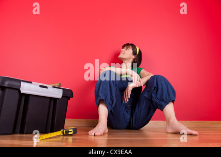 Woman relaxing at sa maison après avoir réparé son mur rouge Banque D'Images