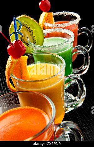 Groupe de quatre verres à vin avec des cocktails sans alcool coloré, décoré avec des fruits et du sucre sur comptoir de bar noir Banque D'Images