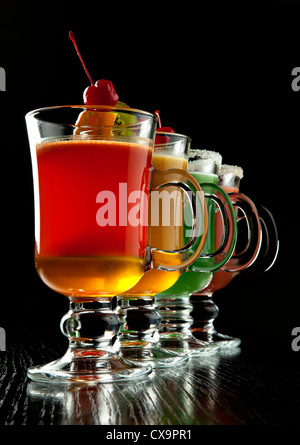 Groupe de quatre verres à vin avec des cocktails sans alcool coloré, décoré avec des fruits et du sucre sur comptoir de bar noir Banque D'Images