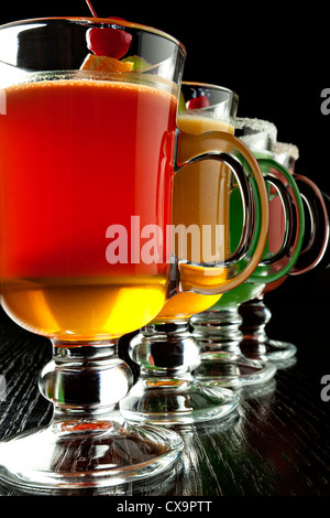 Groupe de quatre verres à vin avec des cocktails sans alcool coloré, décoré avec des fruits et du sucre sur comptoir de bar noir Banque D'Images