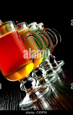 Groupe de quatre verres à vin avec des cocktails sans alcool coloré, décoré avec des fruits et du sucre sur comptoir de bar noir Banque D'Images