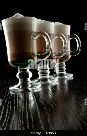 Un groupe de trois verres de cocktails sans alcool en couches chaudes, décoré avec de la mousse de lait sur le comptoir de bar noir Banque D'Images