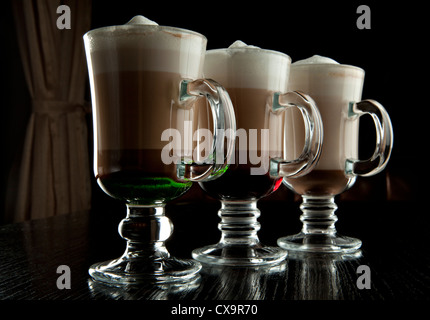 Un groupe de trois verres de cocktails sans alcool en couches chaudes, décoré avec de la mousse de lait sur le comptoir de bar noir Banque D'Images